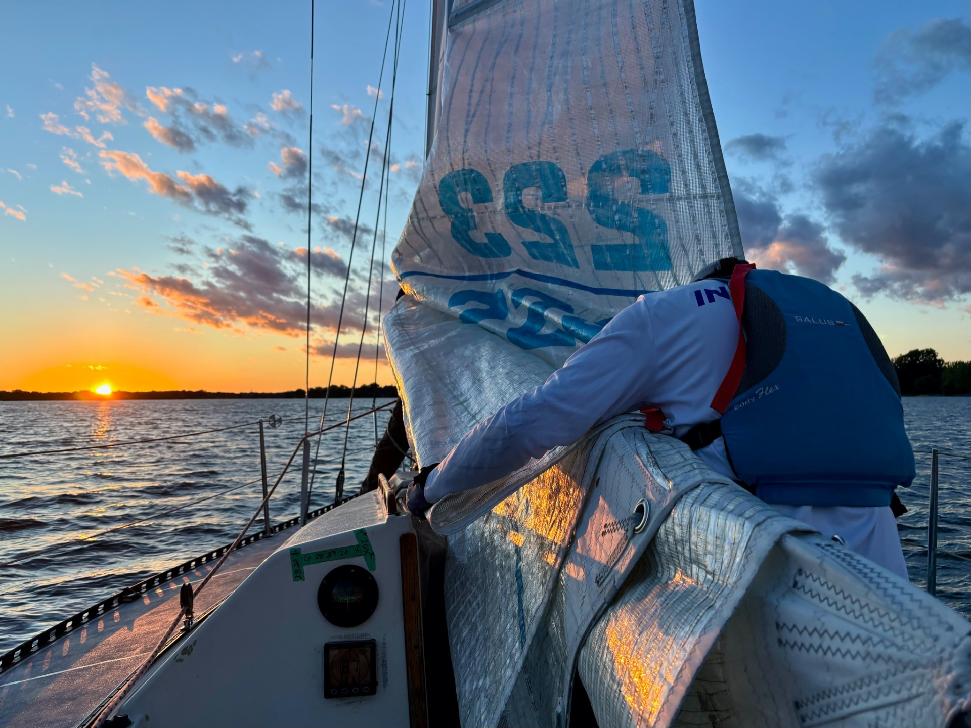 Sailboat underway at sunset with sail handling on deck.